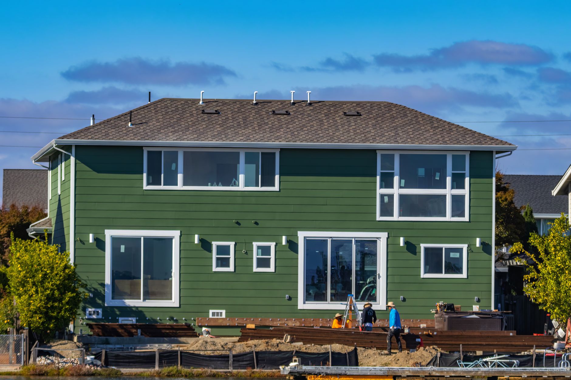 A modern green house under construction with blue skies and workers outside for door and window installation Belleville IL guidance